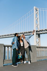 Four people taking a selfie in front of the bay bridge on a sunny day in San Francisco.