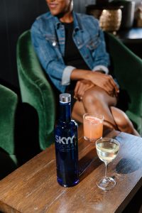 SKYY Vodka bottle with two other cocktails next to it on a wooden table in a bar