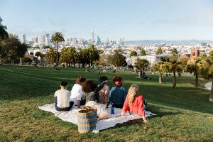 A group of people sitting on a picnic blanket in Dolores Park with a SKYY Vodka bottle behind them as they look out on the view of San Francisco.