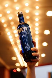 Hand holding a blue SKYY Vodka bottle up in the air with lights from the Castro Theatre back lighting the bottle