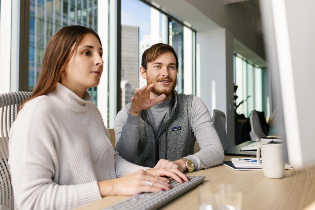 Two Turn River Capital employees collaborating and reviewing charts on a computer